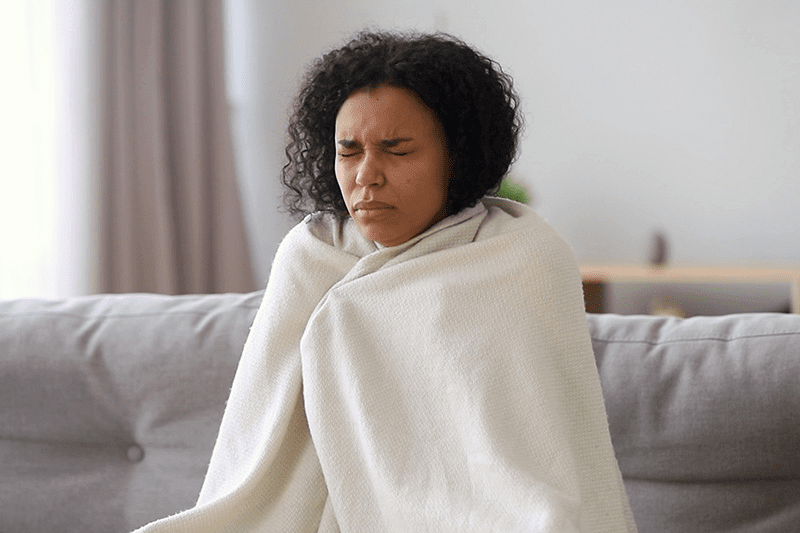 A woman looks uncomfortable while wrapped in a blanket. Upgrade Your Furnace.