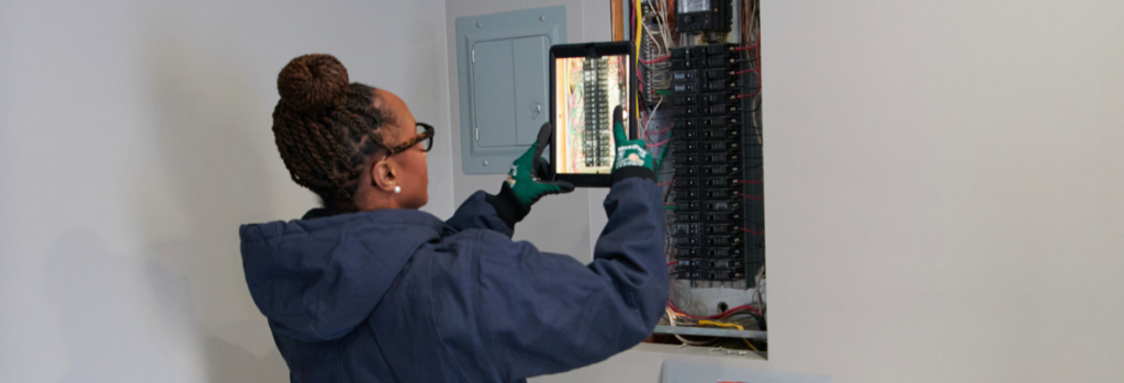 Electrician examining an electrical panel with a tablet