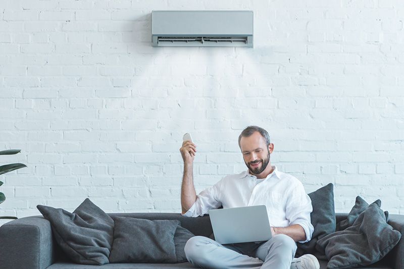 Image of someone sitting on couch with ductless system. Video - 4 Amazing Benefits of Ductless Units.